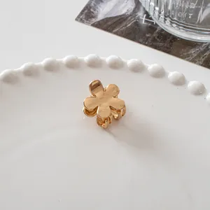 Detailed view of a small golden metal flower hair claw clip on a white ceramic plate