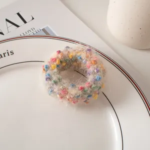Détail d'un chouchou en peluche crème avec pompons colorés posé sur une assiette en céramique
