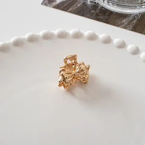 Detail of a small gold bow-shaped metal hair claw clip on a white ceramic plate