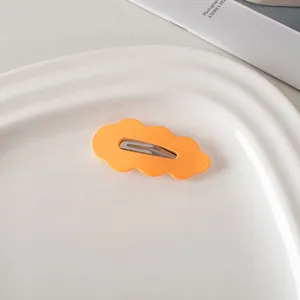 Detail einer orangefarbenen Haarklammer in Wolkenform auf einem weißen Keramiktablett