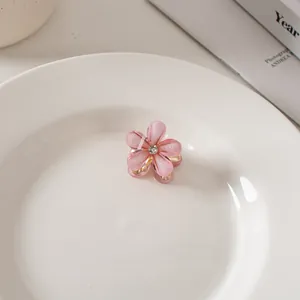 Dettaglio di una mini molletta per capelli a fiore rosa con strass e base in metallo dorato