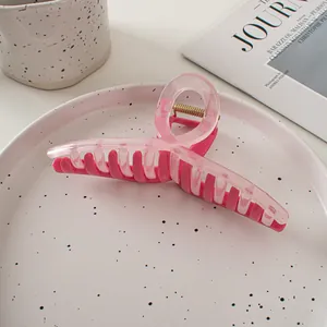 Détail d'une grande pince à cheveux bicolore rose avec ressort doré sur un plateau blanc