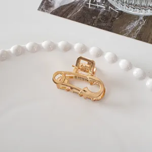 Detail of a golden safety pin hair claw with heart cutout on a white ceramic tray