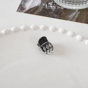 Detailed close-up of a mini black metal hair claw clip on a white ceramic tray