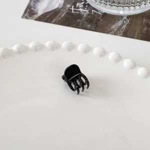 Detail shot of a mini black hair claw clip with a glossy finish on a decorative plate
