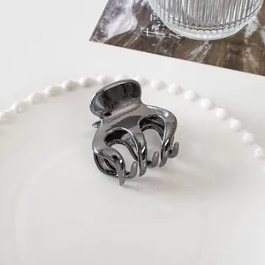 Macro shot of dark gray metal hair claw clip with glossy finish on a white pearl plate