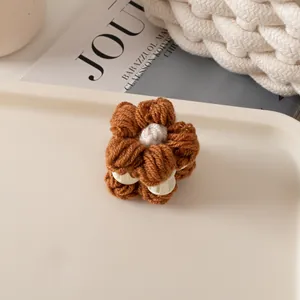 Vue détaillée d'une pince à cheveux fleur tricotée marron sur un plateau minimaliste