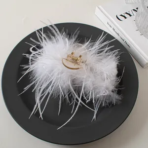 Close-up of a white ostrich feather hair claw clip with gold spring on black display
