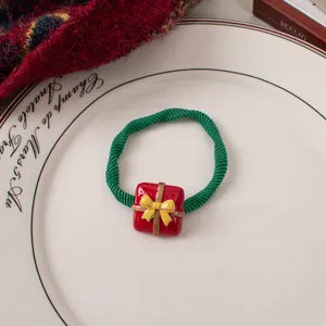 Close-up of green elastic hair tie with a red Christmas gift box charm on a ceramic plate