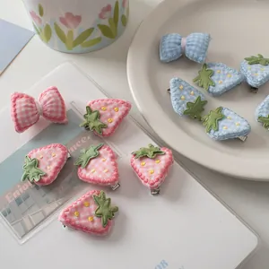 Dettaglio di fermagli per capelli a quadretti rosa e blu con ricamo a fragola e fiocco