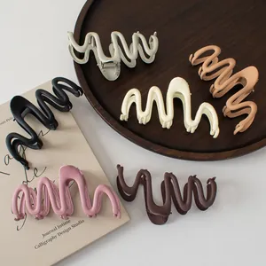 Detailed view of six matte wavy hair claw clips in neutral tones on a wooden tray