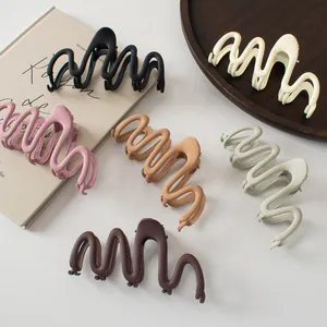 Detail of matte wave-shaped hair claws in Morandi colors on a minimal background