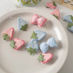 Dettaglio dei fermagli per capelli ricamati a fragola e fiocco in rosa e blu su un piatto