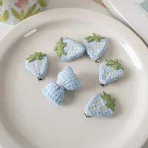 Dettaglio di sei fermagli per capelli ricamati con fragole e fiocchi su un piatto