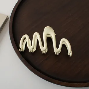Macro shot of large matte cream hair claw clip with a wavy geometric design on a wood tray