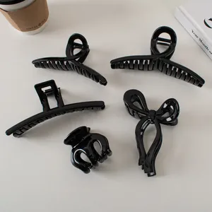 Flat lay of five assorted glossy black claw clips on a minimalist beige desk setup