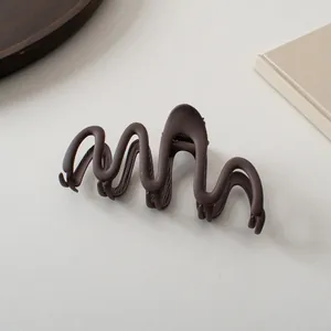 Macro detail of wave-shaped matte dark brown hair claw clip on a minimalist background