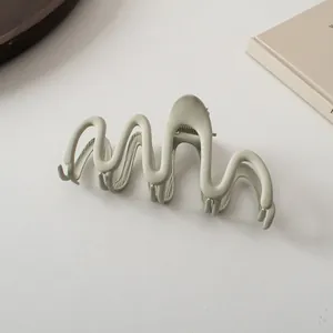 Macro shot of large sage green matte claw clip with elegant wavy design on books