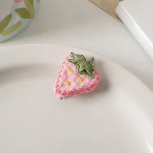 Dettaglio di un fermaglio per capelli a fragola in tessuto rosa con ricamo su un piatto
