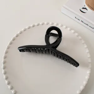 Glossy black hair claw clip with a twisted minimalist design on a white ceramic tray