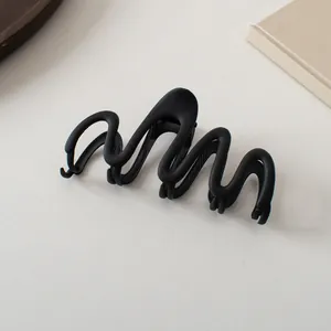Macro detail of wave-shaped matte black hair claw clip with minimalist textured finish