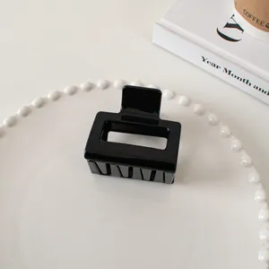 Close-up of a glossy black geometric hair claw clip on a white pearl-edge plate