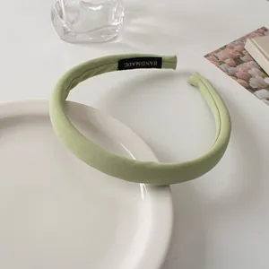 Close-up of light green padded fabric headband with a handmade label on a white table