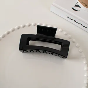 Detail of glossy black rectangular hair claw clip on a tray with lifestyle props