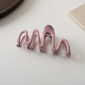 Detail view of wave-shaped mauve matte hair claw clip on minimalist textured background