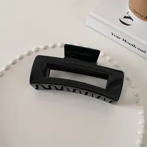 Detail of glossy black hollow rectangular hair claw clip on a minimalist tray
