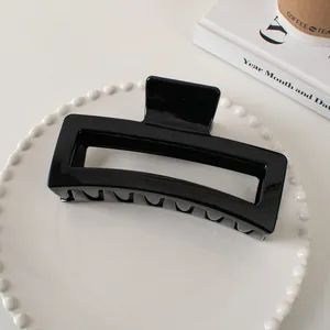 Glossy black rectangular claw clip for thick hair displayed on a modern white tray