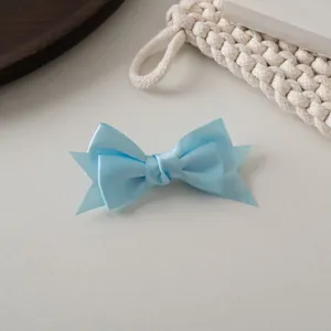 Gros plan détaillé d'une pince à cheveux en satin bleu clair à double nœud sur fond texturé