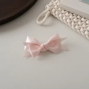 Détail de la pince à cheveux nœud en satin rose montrant la texture lisse et la coupe en queue de poisson
