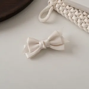 Détail d'une pince à cheveux à double nœud en satin crème avec une texture de soie élégante