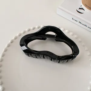 Detailed view of a glossy black hollow wavy hair claw clip on a white ceramic tray