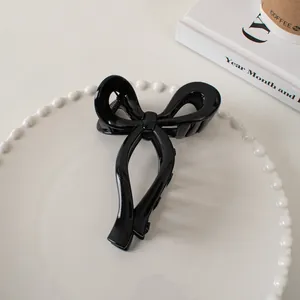 Detail of glossy black bow hair claw clip displayed on a minimalist white ceramic plate