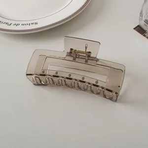 Detail of transparent grey rectangular hair claw clip with metallic spring on white desk