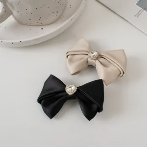 Close-up of beige and black satin bow hair clips with heart rhinestone accents