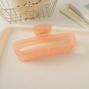 Détail macro d'une pince à cheveux carrée de 13cm couleur pêche dans un décor épuré