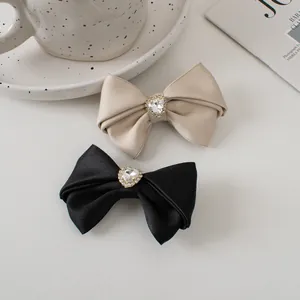 Close-up of elegant satin bow hair clips featuring crystal heart center on smooth fabric