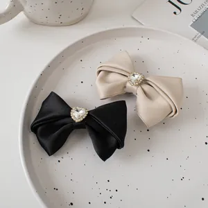 Detail of satin bow hair clips with heart-shaped rhinestones in black and gold colors