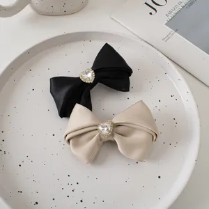 Close-up of black and champagne satin bow hair clips with heart-shaped rhinestones