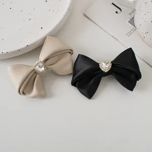 Detail of satin bow hair clips featuring crystal heart embellishments in black and beige