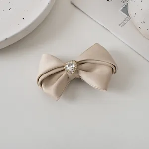Detailed close-up of champagne satin bow hair clip with heart rhinestone decoration