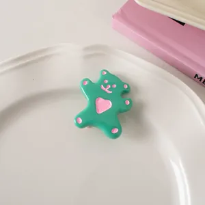 Detail of cute green resin bear hair clip with pink heart on a white tray