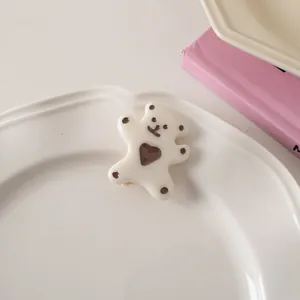 Close-up of a white resin bear hair clip with brown heart detail on a ceramic dish