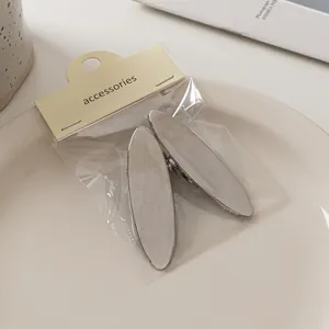 Nahaufnahme von zwei gebürsteten silbernen ovalen Haarspangen in einer Einzelhandelsverpackung