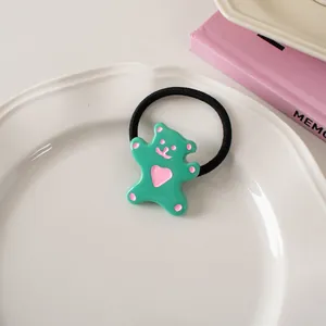 Close-up of mint green bear hair tie with pink heart on a white ceramic tray