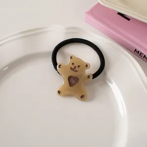 Detail of a black elastic hair tie with a brown translucent bear and hollow heart charm