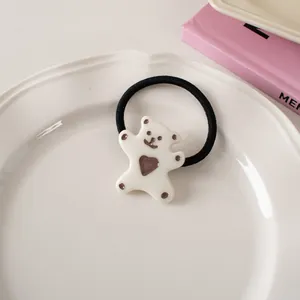 Close-up of a black elastic hair tie with a cute white acrylic bear charm on a ceramic tray